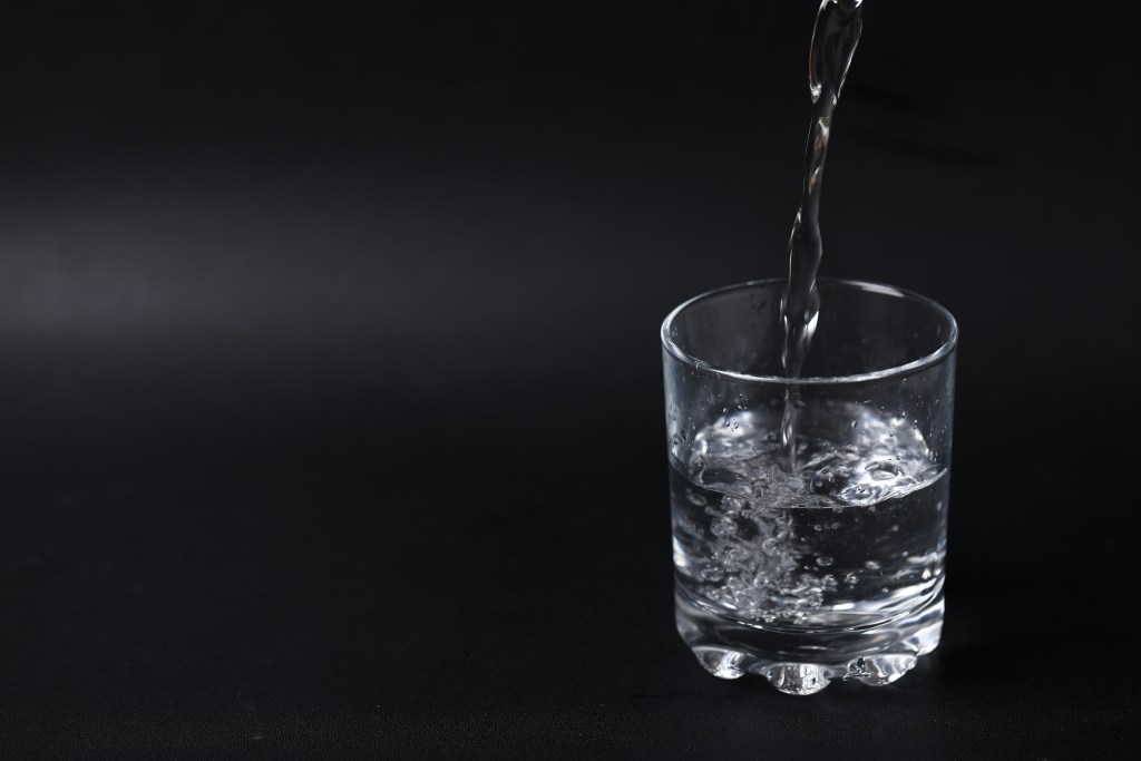 A clear glass being filled with water against a dark background