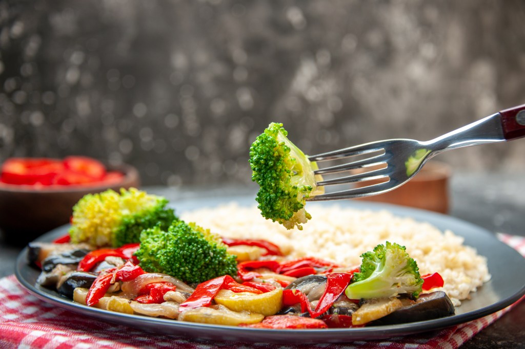 Close-up of a plate of assorted vegetables and rice, with a fork pierced through a broccoli
