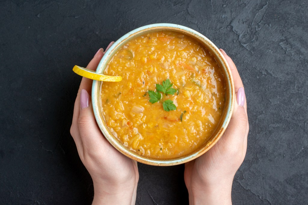 Top view of hands holding yellow dal garnished with lemon & leaves